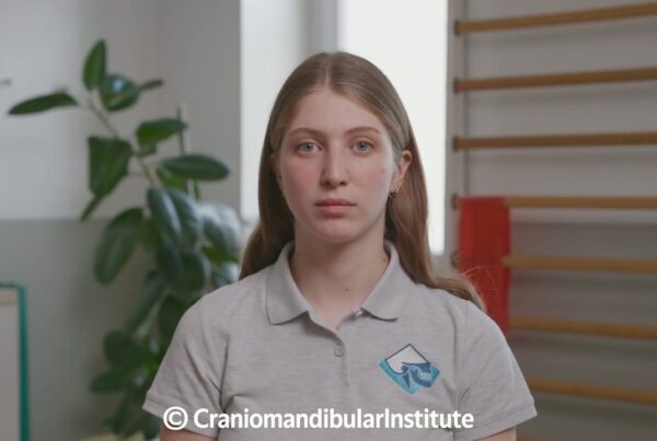 Una giovane donna mostra l’esercizio 3 per il controllo motorio stomatognatico generale in un ambiente clinico