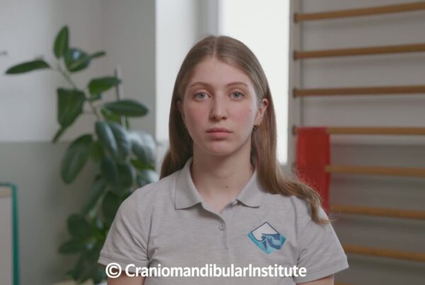 Giovane donna con polo grigia del Cranio Mandibular Institute durante un esercizio di coordinazione mandibolo-cervicale