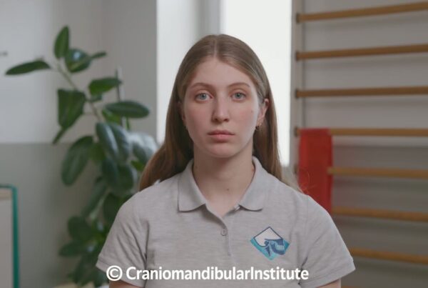 Giovane donna in polo con logo del Cranio Mandibular Institute durante l’esercizio di mobilità laterale mandibolare